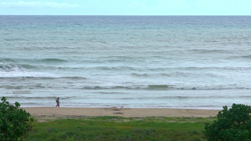 Slowmotion of a woman walking on an empty wild beach on summer vacation. Ocean wave rolling towards sandy beach with green trees of Taiwan island. Sea view of nature background scene. -Dan