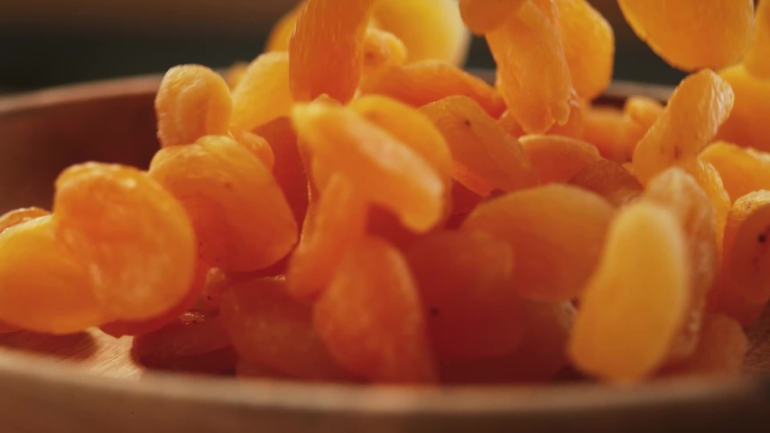 Very Close-up.In a beautiful light, dried apricots  fruit fall into the wooden plate in slow motion.Macro,Phantom Camera, 900 fps video.