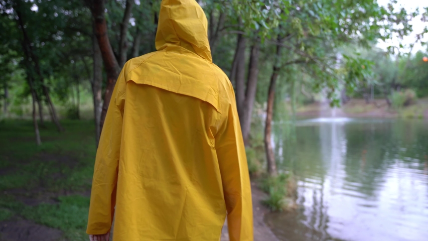A girl in a yellow raincoat walks between the trees along the path. 