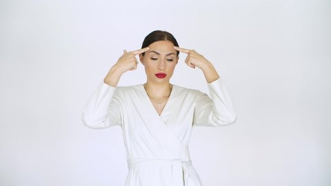 woman in white on a white background points with her fingers to her forehead on her head