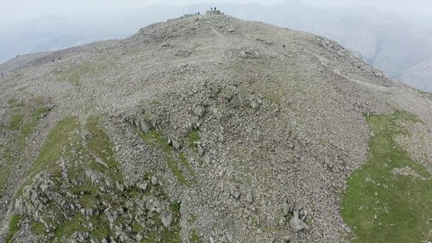 Aerial drone view climbing to reveal people stood on the summit of Scafell Pike, England's biggest mountain