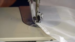 A woman works on a sewing machine. seamstress sews white curtains, close up footage.