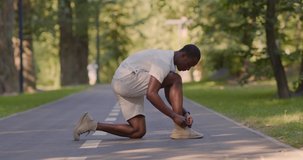 Black sportsman getting ready for morning exercising in park, tying shoelaces on run path
