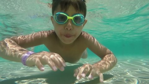 Children in swimming goggles are swimming underwater in the pool
