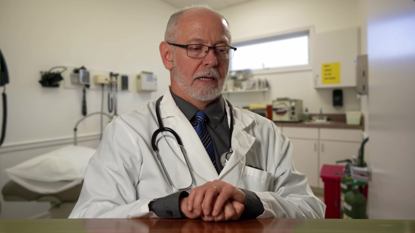 Male doctor wearing a lab coat and stethoscope in exam room sitting at desk dealing with depression or grief. Royalty-Free Stock Footage #1057590718