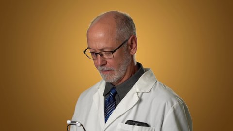 Crazy male doctor doing funny things with stethoscope in comedy on orange background.