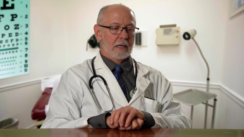 Male doctor wearing a lab coat and stethoscope in exam room sitting at desk dealing with depression or grief. Royalty-Free Stock Footage #1057590802