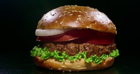 Yummy juicy burger with fresh ingredients rotating in front of camera. Delicious hamburger with grilled beef steak served on chef's table 4k footage close up shot