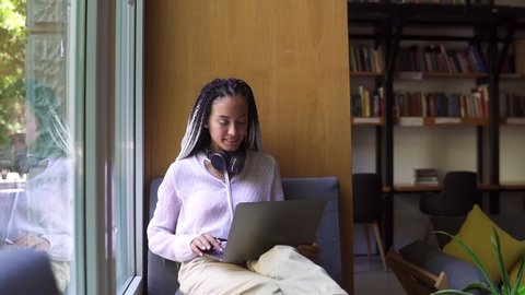 Stylish, dreadlocks student working on laptop at library or workplace. Young female professional working on computer device. Remote freelance work or studying - focused and concentrated. Wearing white