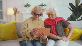 Beautiful elderly women couple of stylish grannies using tablet application for remote communication waving hand talking on webcam with friends online. Fashion grandmas. Digitalization.