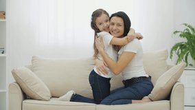 Lovely mother and beautiful daughter sitting on the sofa, hugging, smiling.