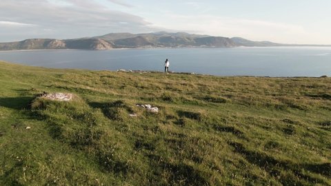 Aerial footage of young girl on bike atop scenic Great Orme, beautiful mountain cliff edge near coastal town Llandudno, North Wales near Snodownia National Park. Mountain and Ocean View.