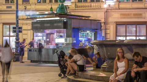 Street food kiosk and sausage stand night timelapse in Vienna. People buying food with drinks and eating around