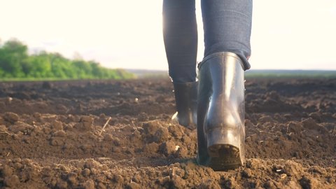 agriculture. woman farmer in rubber boots walks on black soil beautiful sunshine sunset. girl worker walks lifestyle on agricultural dirt ground land