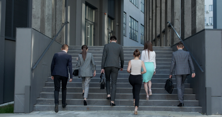 Rear view of Six Business People Walking up the Stairs. Men and women in formal suits going up stairs into office building. Partnership, communication business people concept. Royalty-Free Stock Footage #1057607914