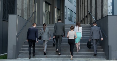 Rear view of Six Business People Walking up the Stairs. Men and women in formal suits going up stairs into office building. Partnership, communication business people concept.