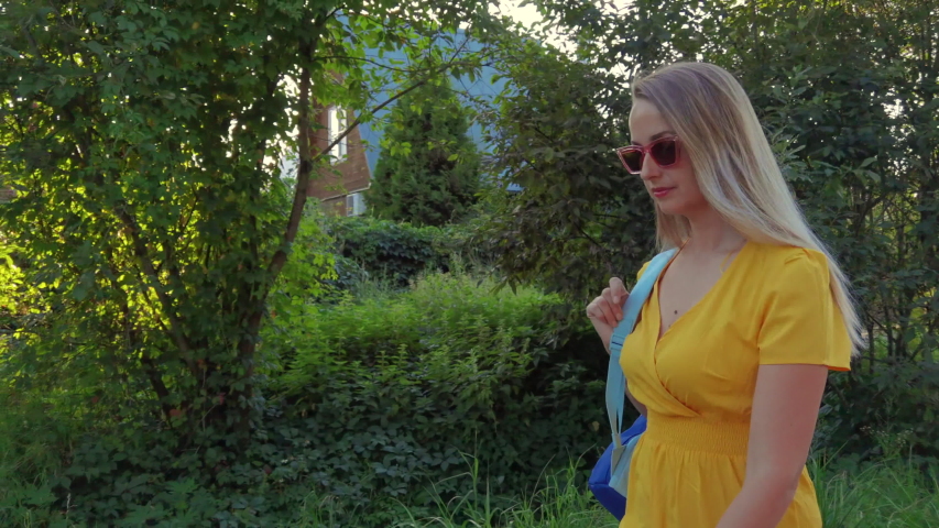 Woman in yellow dress and sunglasses walking on the road in rural landscape