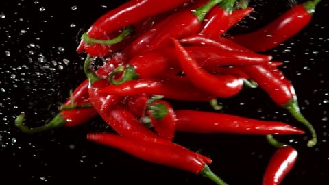 Super slow motion of coloured chilli peppers in collision, red background. Filmed on high speed cinema camera, 1000 fps
