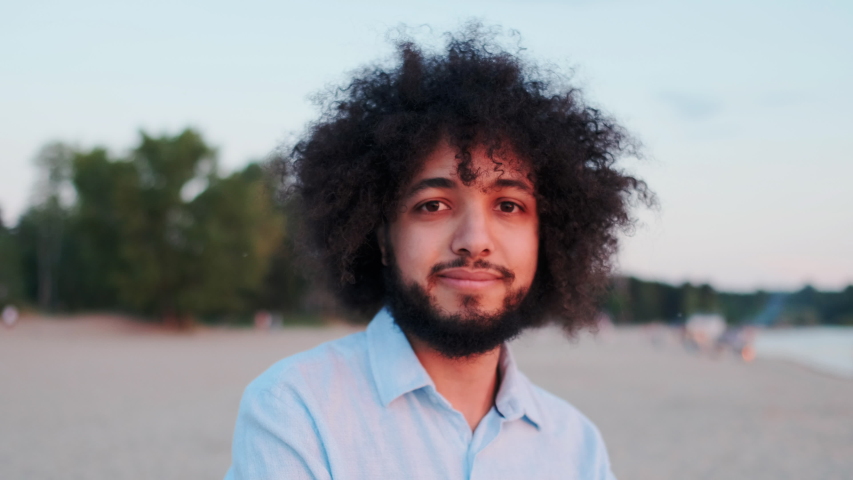 Handsome Curly Hispanic Man Looking in Camera while Standing Alone in Park Outside. Attractive Curly Man with Beard and Stylish Hairdo Enjoying Successful Lifestyle. Closeup Portrait. | Shutterstock HD Video #1057614235