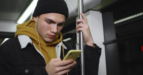 Crop view of young man using his modern moilephone while going on subway. Handsome male student looking and phone screen while browsing internet. Concept of technology