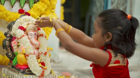 Little girl Kid offering flowers on Ganesha Idol before praying in front of god during Ganesha or vinayaka Chaturthi festival ceremony