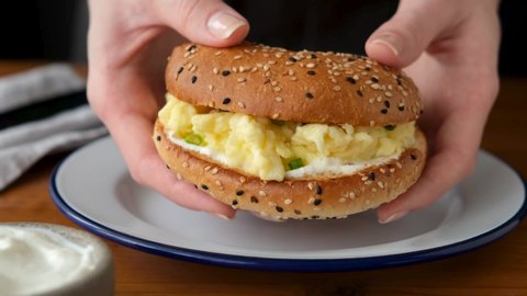 Sesame bagel sandwich with scrambled eggs in female hands. Tasty juicy breakfast meatless burger