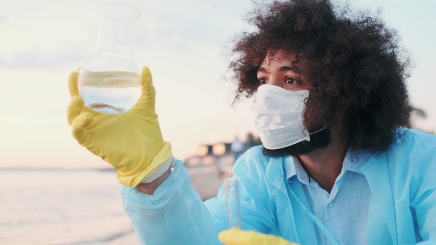 Male Ecologist or Biologist with Glass Test Tubes Examine Level of Water Pollution on Lake. Protective Gloves, Medical Mask and Robe. Damage of Human, Eco Conservancy. Closeup. Royalty-Free Stock Footage #1057618981