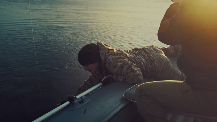 Friends fishing. Two amateur anglers fishing from the boat and fighting with trophy fish. Fishing rod bends under the big fish