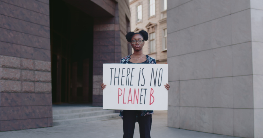 Young african american woman holding there is no planet b cardboard while standing at city street. Female activist supporting eco campaign. Concept of environmental protection. Zoom in. Royalty-Free Stock Footage #1057621036