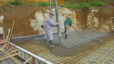 LJUBLJANA, SLOVENIA, APRIL 2020: Crew of experienced builders pours a concrete slab at a construction site. Contractors pour wet mortar over rusty wiring while building the foundation of a house.