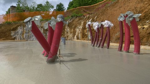 CLOSE UP: Large freshly poured concrete slab dries in the warm spring sunshine. Red installation tubing sticks out of a thick layer of mortar drying at a construction site. Fresh house foundation.