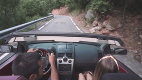 Young adult couple driving a convertible luxury car outdoors around mountains and forests in Spain. People enjoying freedom and nature during summer holidays. Sports car stock video footage.