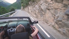 Young adult couple driving a convertible luxury car outdoors around mountains and forests in Spain. People enjoying freedom and nature during summer holidays. Sports car stock video footage.
