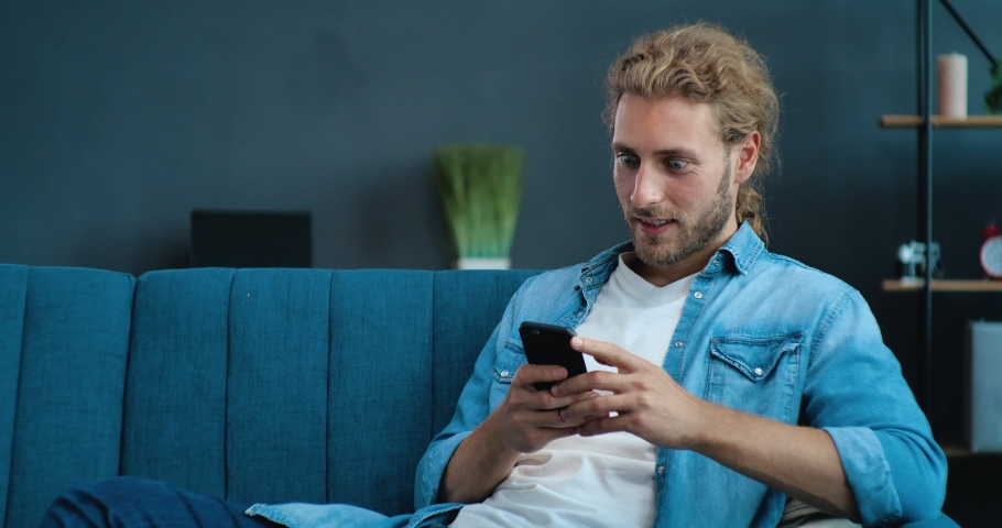  Happy Man celebrating mobile win uses Phone at home office. Man reading good news, Victory while sitting on couch Royalty-Free Stock Footage #1057627729
