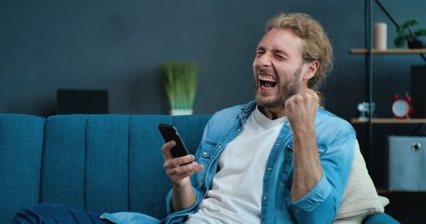 Portrait of happy businessman enjoying Success on Mobile Phone at home office. Closeup joyful Guy reading good news on Phone in slow motion. Surprised Man celebrating Victory on phone in Apartment.