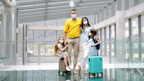 Long shot of family with two children going on holiday, wearing face masks at the airport.