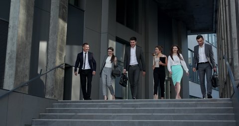 Confident team members walking on stairs. Business men and women in formal suits go and talk on the background of modern office building.