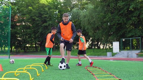 Attractive brisk 13-aged football players training together on the sport field with artificial grass covering and following clear instructions of professional trainer,4k