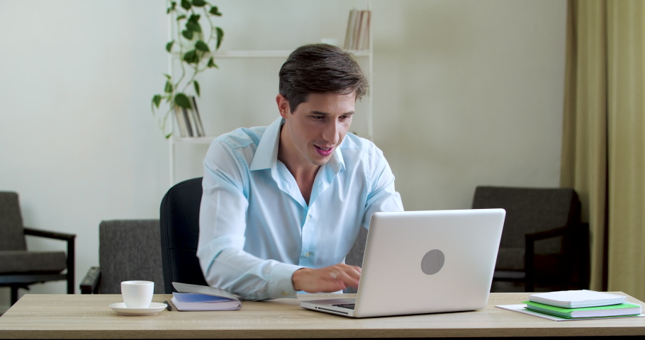 Overjoyed young IT specialist businessman looking at laptop screen, excited by unbelievable good news. Happy office worker emotional executive celebrating successful investment, obtaining financing Royalty-Free Stock Footage #1057635358