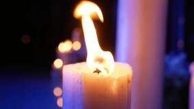 Close-up shot of a large burning candle with purple neon illuminated background. Colorful video background with burning candles.