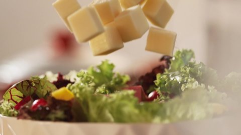 Very Close-up, 900 fps video.Slow motion diced cheddar cheese is thrown onto a delicious salad with fresh lettuce and cherry tomatoes.Macro,Phantom Camera.