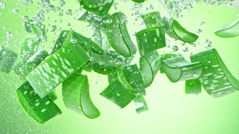 Super Slow Motion Shot of Aloe Vera Cuts Falling into Water on Green Background at 1000fps.