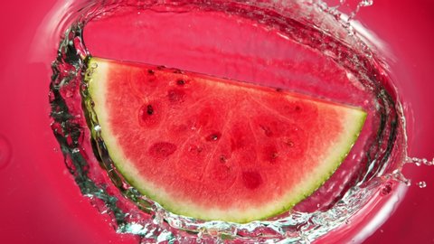 Super Slow Motion Shot of Falling Fresh Watermelon Slice into Water on Red Background at 1000fps.