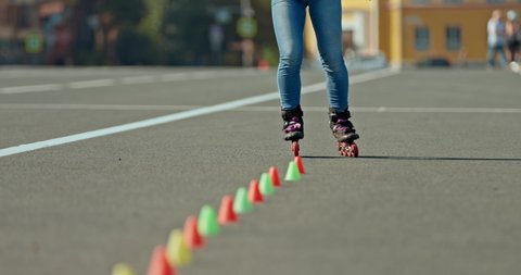 Legs of an athlete in roller skates go around the cones, freestyle butterfly. Professional freestyle in roller skates, cones are in a row. 4k, 10bit, ProRes