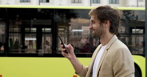 Happy handsome man in business suit checking arrival time of public transport on smartphone. Bearded guy waiting for bus and using modern device.