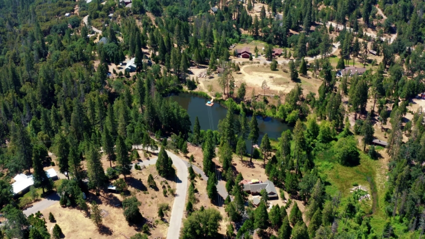 Aerial drone shot of a small lake surrounded by pine trees near the larger Bass Lake south of Yosemite in Northern California on a warm summer day.