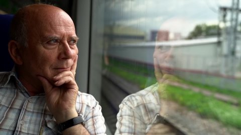 elderly man is looking at window of moving suburban train, travelling passenger