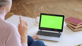 Elderly mature woman with gray hair and a video call on her Laptop. Laptop with a green screen