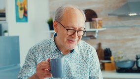 Cheerful senior man during video conference in kitchen while enjoying breakfast and a cup of coffee. Elderly person using internet online chat technology video webcam making a video call connection - Powered by Shutterstock - Get 15% off with code: PIKWIZARD15