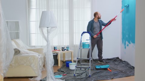 Young man painting wall with roller brush while renovating his apartment. Handyman redecoration and home construction while renovating and improving. Repair and decorating.